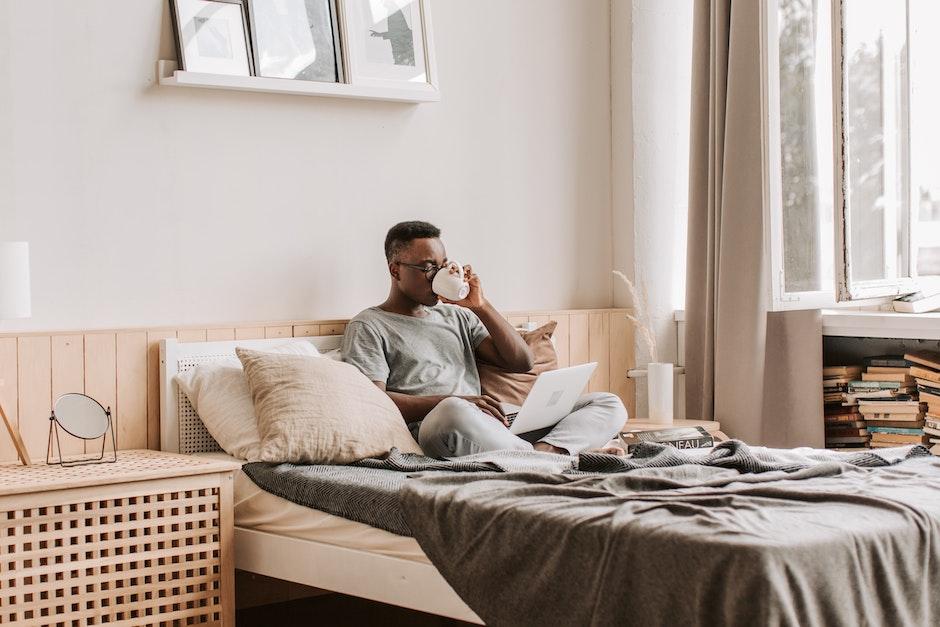 Man in Gray Shirt Sitting on Bed while Drinking Coffee