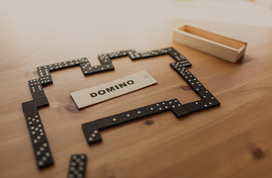 Arrangements of small black dominoes with white dots on surface and wooden box on table in sunlight