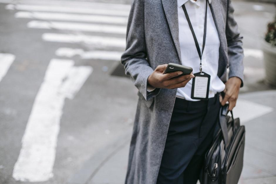 From above of crop anonymous female entrepreneur wearing stylish gray coat with badge and laptop in 