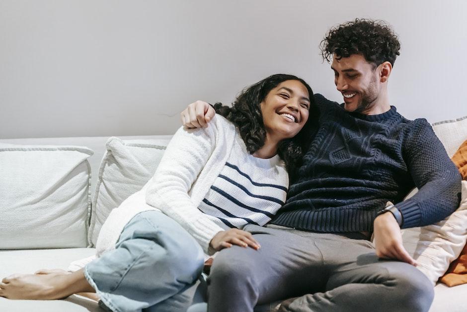 Happy barefoot African American girlfriend with closed eyes and ethnic boyfriend hugging on sofa in 