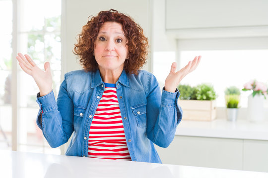 Middle age senior woman with curly hair wearing denim jacket at home clueless and confused expressio