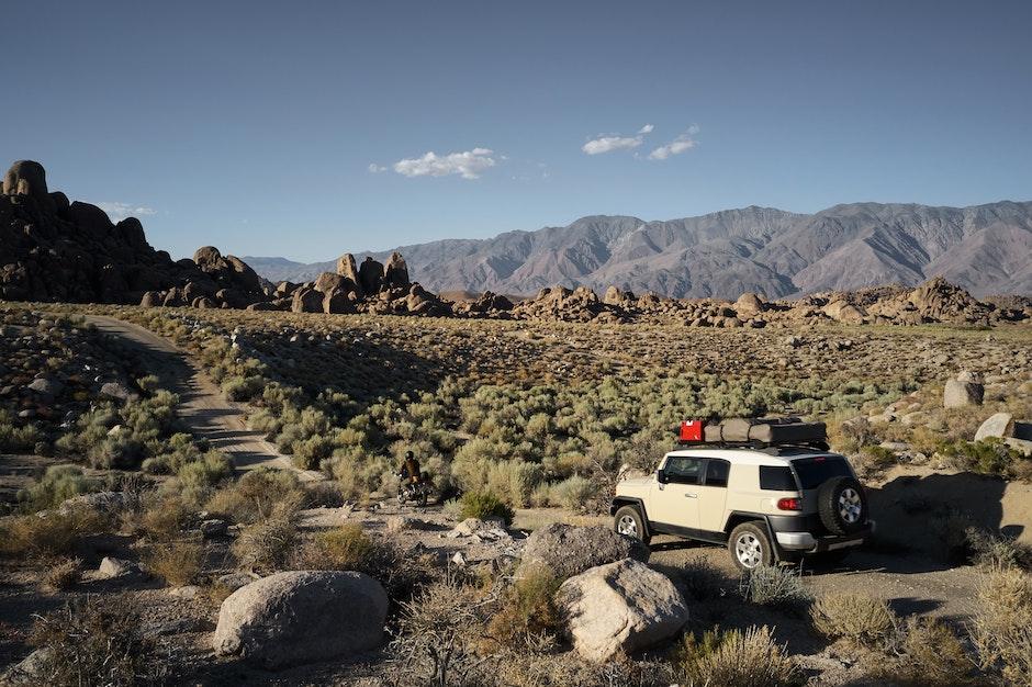 Picturesque view of SUV and motorbike driving on dusty narrow road in mountainous semidesert terrain