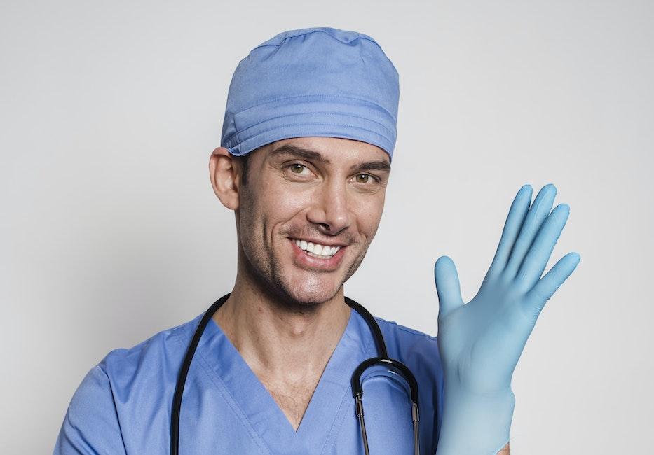 Smiling man in medical clothes pulling on sterile gloves